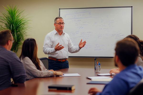 Group of professionals in a meeting with technical drawings on a whiteboard.