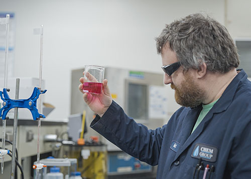 A man examining a red chemical in a glass jar.