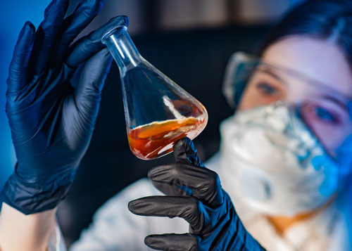 chemical-quality-control-500 Woman examining red chemical in glass beaker.