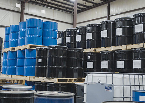 Stacks of large blue and black drums filled with chemicals ready for distribution.