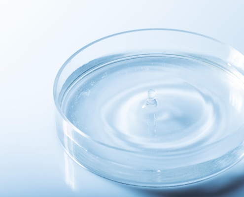 A clear liquid dropping into a small glass dish.
