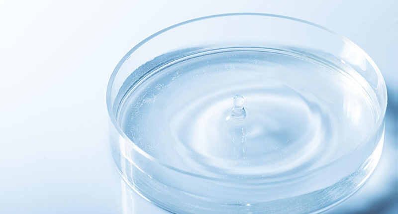 A clear liquid dropping into a small glass dish.