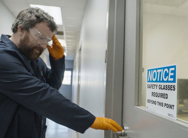 A man in full safety gear about to enter a door with a safety warning on it.