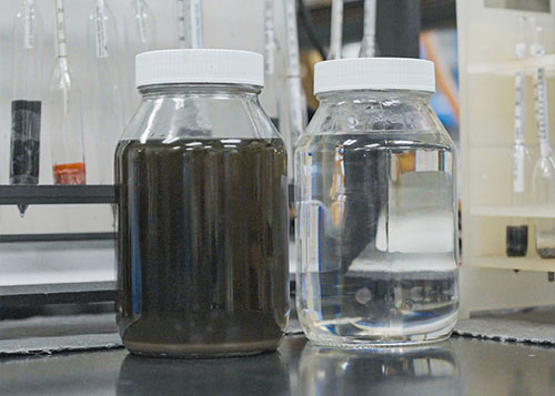 Two glass jars on a table filled with chemicals. One with a brown liquid and one with a clear liquid.