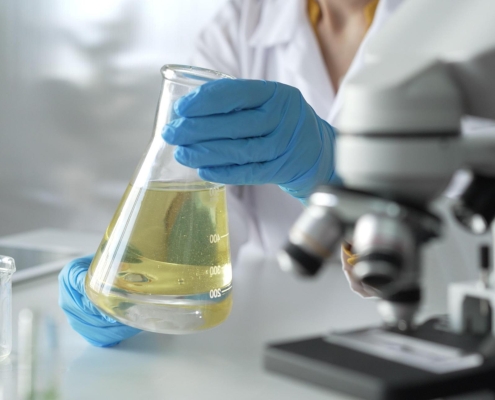 Woman holding large glass beaker filled with yellow chemical liquid.